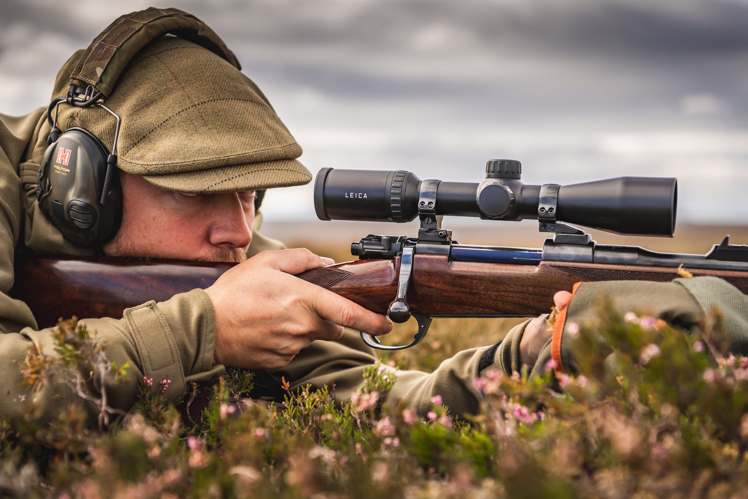 Man laying in heather and looking through rifle scope